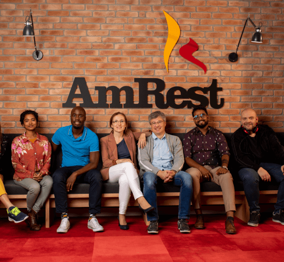 Diverse team of professionals sitting together at AmRest headquarters with company logo on brick wall background